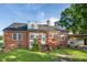 View of brick home's backyard featuring a well-manicured lawn, patio, and mature trees at 201 N Us 301, Micro, NC 27555