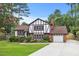 Charming Tudor-style home with brick and white facade, lush lawn, and a paved driveway leading to a garage at 2020 Port Royal Rd, Raleigh, NC 27609