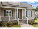 Charming covered front porch with stone-accented stairs and decorative railing at 75 Woodbark Cv # 10, Willow Springs, NC 27592