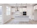 Contemporary white kitchen with a large window, stainless steel hood, and sleek countertops at 370 Fast Pitch Ln, Four Oaks, NC 27524