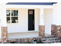 Inviting front porch with stone-clad columns and steps, leading to a black front door with sidelight window at 818 Barbour Farm Ln, Four Oaks, NC 27524