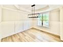 Bright dining room with wainscoting, modern chandelier, tray ceiling, and wood-look floors at 2613 Silver Gate Ct, Wake Forest, NC 27587