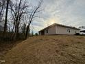 A view of the home's exterior, showing its placement on a lot with natural surroundings and a gently sloping hill at 55 Capeside Ct, Lillington, NC 27546