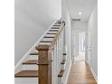 Hallway with wood floors and a staircase featuring a wood handrail and white risers, leading to an open doorway at 2038 Fishamble St, Fuquay Varina, NC 27526