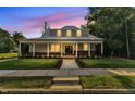 Inviting home with a metal roof, brick accents, and a welcoming front porch at dusk with lit windows at 505 S Magnolia Ave, Dunn, NC 28334