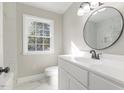 Bright bathroom with a large round mirror, modern vanity, and marble tiled floor and shower at 203 W Stewart St, Coats, NC 27521