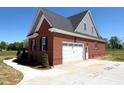 Side view of a brick home featuring a white garage door, concrete driveway, and meticulously maintained landscaping at 7575 Sweetwater Dr, Nashville, NC 27856