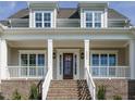 Charming front porch featuring brick accents, white railings, and a stained wood front door at 1233 Azalea Garden Cir, Raleigh, NC 27603