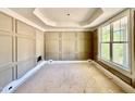 Living room with decorative paneled walls, large window, tray ceiling, and unfinished floors at 2624 Silver Gate Ct, Wake Forest, NC 27587