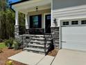 Inviting front porch with stone accents, a black railing, and access to a two car garage at 262 Grand Griffon Way, Lillington, NC 27546
