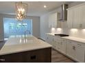 Modern kitchen featuring white cabinets, a large island with sink, stainless steel vent hood, and contemporary lighting at 55 New Liberty Dr, Youngsville, NC 27596