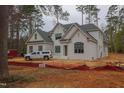Two-story white brick home with black framed windows and dark roof, set in a wooded area undergoing construction at 6805 Greystone Dr, Raleigh, NC 27615