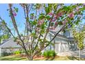View of the home and detached garage through a flowering tree, with a lush green lawn and manicured landscaping at 2721 Sanctuary Woods Ln, Raleigh, NC 27606