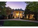 Elegant home with impressive columns, lush landscaping, and a circular driveway, glows under the evening sky at 11201 Jonas Ridge Ln, Raleigh, NC 27613