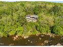 Aerial view of a modern home with a pool surrounded by lush forest and bordered by the river at 196 Paces Mill Trl, Pittsboro, NC 27312