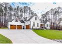 White farmhouse with three-car garage, stone accents, and a long driveway at 257 Rawhide Dr, Louisburg, NC 27549