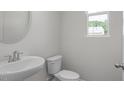 Modern half bathroom with a pedestal sink, toilet, and a round mirror at 3854 Well Fleet Drive, Fuquay Varina, NC 27526