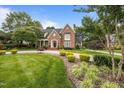 Stately brick home with lush landscaping, circular driveway, and mature trees under a blue sky at 2035 Stuart Ct, Burlington, NC 27215