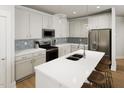 Bright kitchen features white cabinets, stainless appliances, island with seating, and tile backsplash at 257 Beacon Dr, Pittsboro, NC 27312