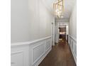 Hallway featuring decorative wainscoting, wood floors, stylish light fixture, and access to kitchen at 47 Highmeadow Ln, Clayton, NC 27520