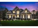 Beautifully lit two-story home with manicured lawn, stone accents, and inviting front porch at dusk at 1100 Kingwood Dr, Raleigh, NC 27609