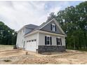 Side view of gray house features a white garage door, stone accents, and lush green trees at 1663 Keith Hills Rd, Lillington, NC 27546