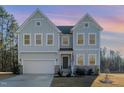 Charming two-story home at dusk, featuring stone accents, a two-car garage, and a welcoming front porch with an American flag at 25 Courrone, Willow Springs, NC 27592