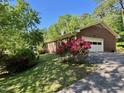 Side view of a brick home featuring an attached garage, blooming bushes, and a well-maintained lawn and driveway at 2118 N Woodland Rd, Henderson, NC 27536