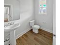 Cozy half bath features a pedestal sink, a toilet, and wood flooring; the bathroom is well-lit at 120 Whistling Way # Cary Traditiol, Lillington, NC 27546
