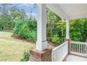 View from the covered porch with white columns and railings, overlooking the serene, wooded surroundings at 1354 Red Bud Ct, Wake Forest, NC 27587