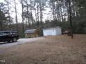 Two outbuildings offer versatile storage space on a wooded lot; black car parked nearby at 2506 Poole Rd, Raleigh, NC 27610