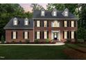 A two-story brick home with black shutters is illuminated by the warm glow of twilight at 102 Legault Dr, Cary, NC 27513