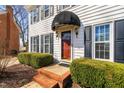 Close-up of a home's entrance with red door, awning, brick steps, and manicured hedges at 3523 Elk St, Burlington, NC 27215