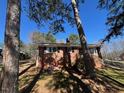 Cozy brick home nestled among tall pine trees on a sunny day with a clear blue sky above at 1220 Roanoke Ave, Henderson, NC 27536