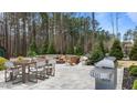 Outdoor patio featuring a fire pit, dining area, and built in grill overlooking a wooded area at 8816 Knights Union Way, Wake Forest, NC 27587