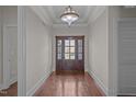 Bright foyer featuring hardwood floors, elegant lighting, and a striking wooden door with decorative glass panels at 1637 Hasentree Villa Ln, Wake Forest, NC 27587