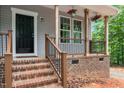 Close up view of the welcoming front porch that features hanging flower baskets and brick base and wooden stairs at 5507 Eagles Nest Trl, Snow Camp, NC 27349