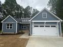 Charming blue single-story home featuring a two-car garage and a well-manicured front yard surrounded by tall trees at 9231 Bear Run Ln, Middlesex, NC 27557