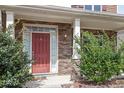 Stone accented porch featuring a red front door flanked by sidelights and decorative shrubs at 5029 Stonewood Pines Dr, Knightdale, NC 27545