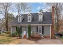 Charming home featuring dormer windows, mature trees, and a brick chimney, offering a classic and inviting curb appeal at 7017 Sandringham Ct, Raleigh, NC 27613