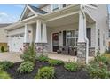 Inviting front porch featuring stone columns, seating, a festive wreath, and landscaped garden beds at 1725 Langlais Dr, Graham, NC 27253