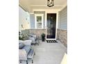 Cozy covered front porch with stone accents, seating area, welcome mat, and a black front door at 225 Ivy Arbor Way, Holly Springs, NC 27540