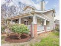 Side exterior showcasing the covered porch, brick pillars, and established landscaping, highlighting the home's charm at 1426 N Roxboro St, Durham, NC 27701