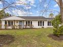 Beautiful single-story house with white brick and dark shutters, complemented by a vibrant green lawn and blooming bushes at 711 Wheat Mill Rd, Durham, NC 27704