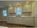 Well-lit kitchen featuring white cabinets, a tiled backsplash, and stainless steel sink at 1421 Deer Crossing Ct, Henderson, NC 27536
