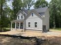New two-story home with gray siding, black roof, and a covered front porch surrounded by wooded landscape at 5036 Trotter Dr, Raleigh, NC 27603