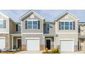 A lovely exterior shot of new townhomes featuring light colored siding, black shutters, and one car garages at 267 Canopy Dr, Graham, NC 27253