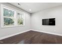 This room features a wall mounted television, dark wood floors, and two large windows letting in natural light at 109 Belle Plain Dr, Morrisville, NC 27560