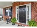 Charming brick home featuring a black front door, inviting porch with rocking chairs, and lush greenery at 717 Maple Brook Rd, Fuquay Varina, NC 27526