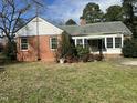 A charming, brick home with a covered porch, surrounded by greenery and a lush lawn under a cloudy sky at 1101 W Divine St, Dunn, NC 28334